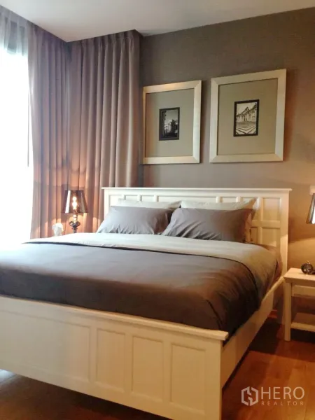 Condominium for rent in Khlong Toei, Bangkok - Cozy master bedroom with white bed frame, gray bedding, framed artwork and wood floors.