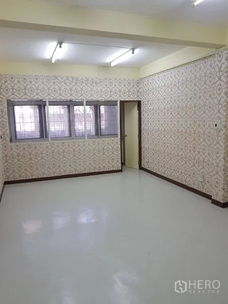 Retail Space for rent in Khlong Toei, Bangkok - Bright empty retail room with patterned wallpaper, barred windows and fluorescent ceiling lights over a glossy floor.