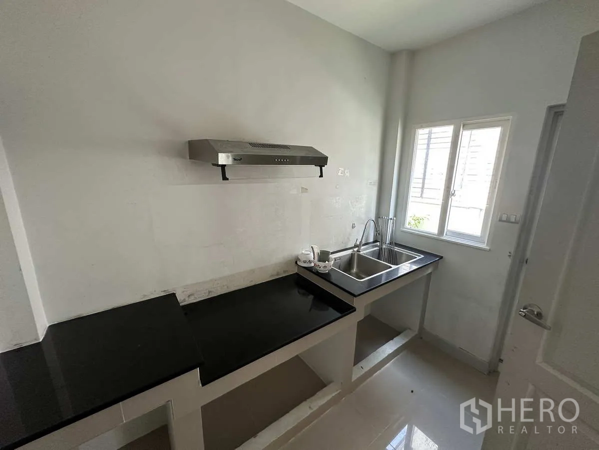 Detached House for rent in Khlong Luang, Pathum Thani - Compact Thai kitchen with black stone countertops, double sink and cooker hood.