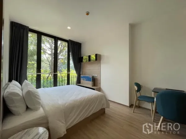 Condominium for sale in Watthana, Bangkok - Bedroom with double bed, study desk, and tall windows facing tree views.
