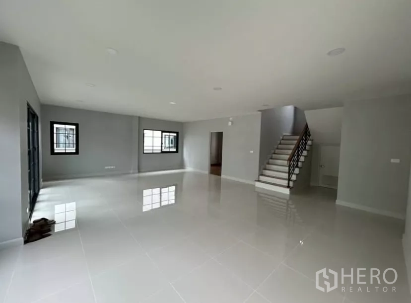 Detached House for rent in Bang Phli, Samut Prakan - Wide living area view showing stairs, multiple windows and neutral gray walls.