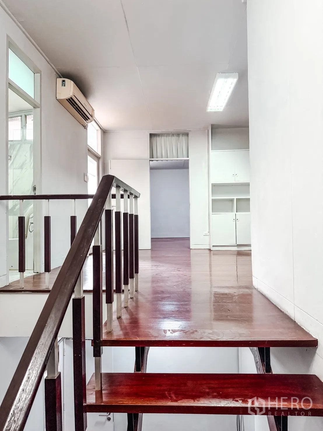Home Office for rent in Watthana, Bangkok - Dark wood staircase and handrail ascending to an upper landing with cabinets and an air conditioner.
