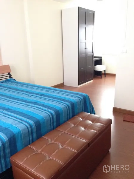 Detached House for sale in Phra Khanong, Bangkok - Second bedroom featuring blue bedding, a freestanding wardrobe and a padded bench.