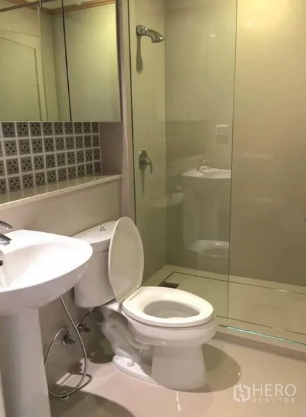 Condominium for rent in Khlong Toei, Bangkok - Compact bathroom with pedestal sink, toilet and glass-enclosed shower.