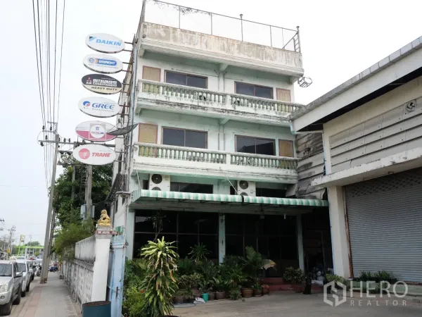 工厂 出租或出售在Bang Khun Thian, Bangkok - 3.5层商业办公楼正立面，带雨棚与卷帘门，紧邻厂房。