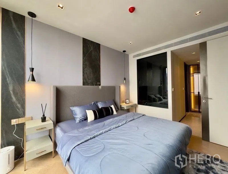 คอนโด for rent or sale in Watthana, Bangkok - ห้องนอนสไตล์โมเดิร์นพร้อมหัวเตียงบุผ้า โคมไฟห้อย และโต๊ะข้างเตียง