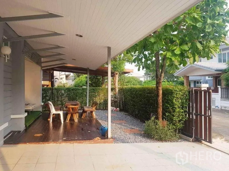 Detached House for sale in Nonthaburi - Covered patio with wooden deck seating, gravel path and a gated front garden.