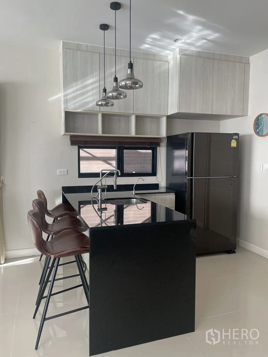 Detached House for rent or sale in Lam Luk Ka, Pathum Thani - Kitchen island breakfast bar with three stools, black countertop and pendant lighting next to the fridge.