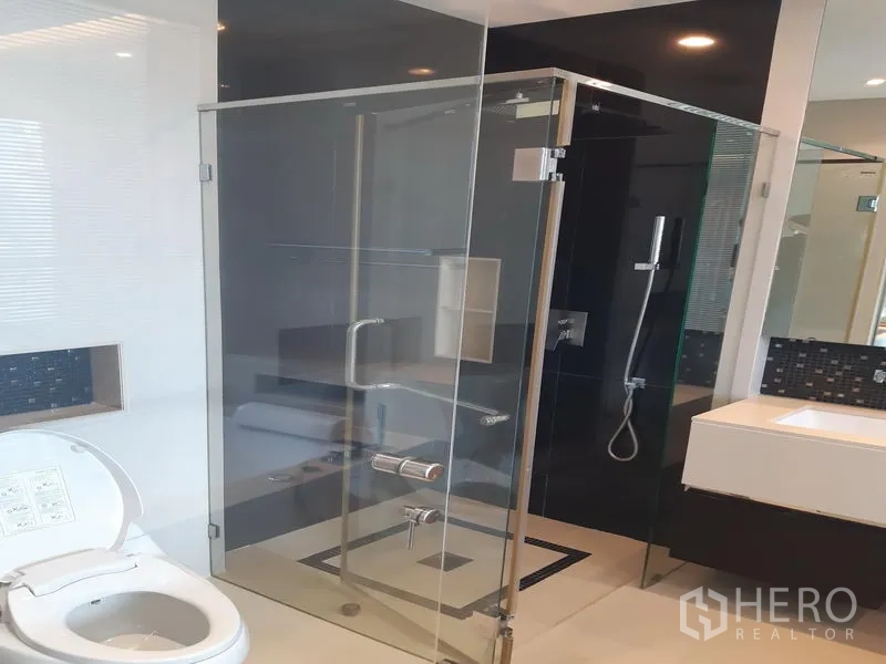 Condominium for rent in Khlong Toei, Bangkok - Glass-enclosed shower, toilet and sleek vanity in a bright bathroom.