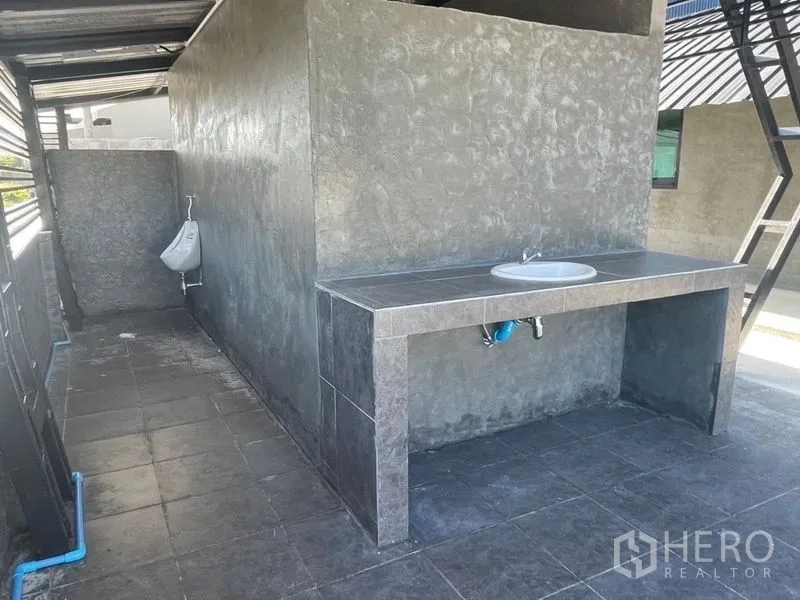 货栈 出租在Ban Bueng, Chon Buri - 近景：铺砖的清洗区，带洗手池与小便器，位于遮蔽棚下。