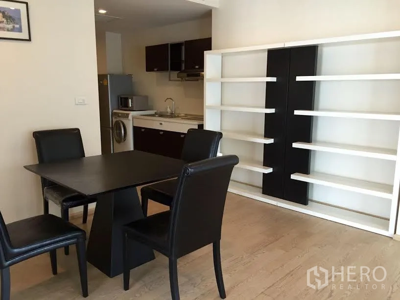 Condominium for rent or sale in Khlong Toei, Bangkok - Open-plan dining area with four-seat table, white shelving, and a compact kitchenette in the background.