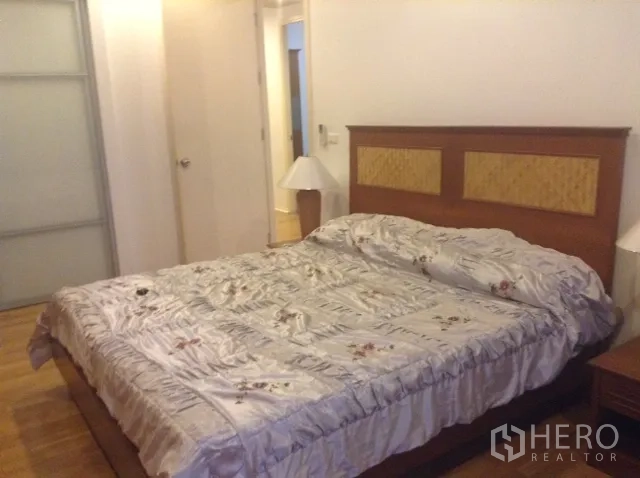 Condominium for rent or sale in Din Daeng, Bangkok - Spacious bedroom angle showing wooden floors, a king bed, nightstands, and a sliding wardrobe door.