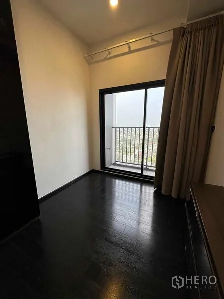 Condominium for rent in Khlong Toei, Bangkok - Empty room with dark wood floors and sliding glass door to a small balcony with city view.