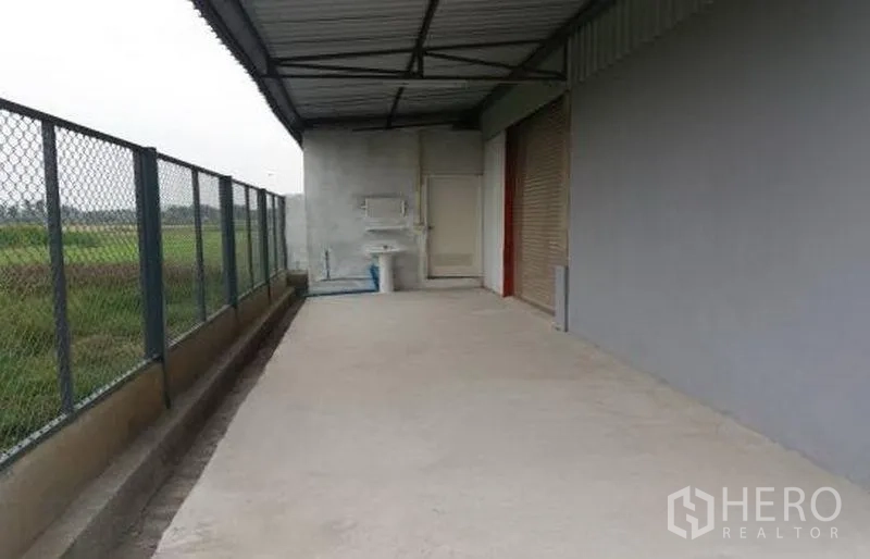 Factory for rent in Pathum Thani - Covered rear service zone with sink, roller door, and fenced perimeter walkway.