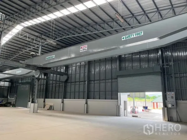 Warehouse for rent in Bang Phli, Samut Prakan - High‑ceiling warehouse interior featuring overhead bridge crane beams, metal roof skylights and a roller shutter door.