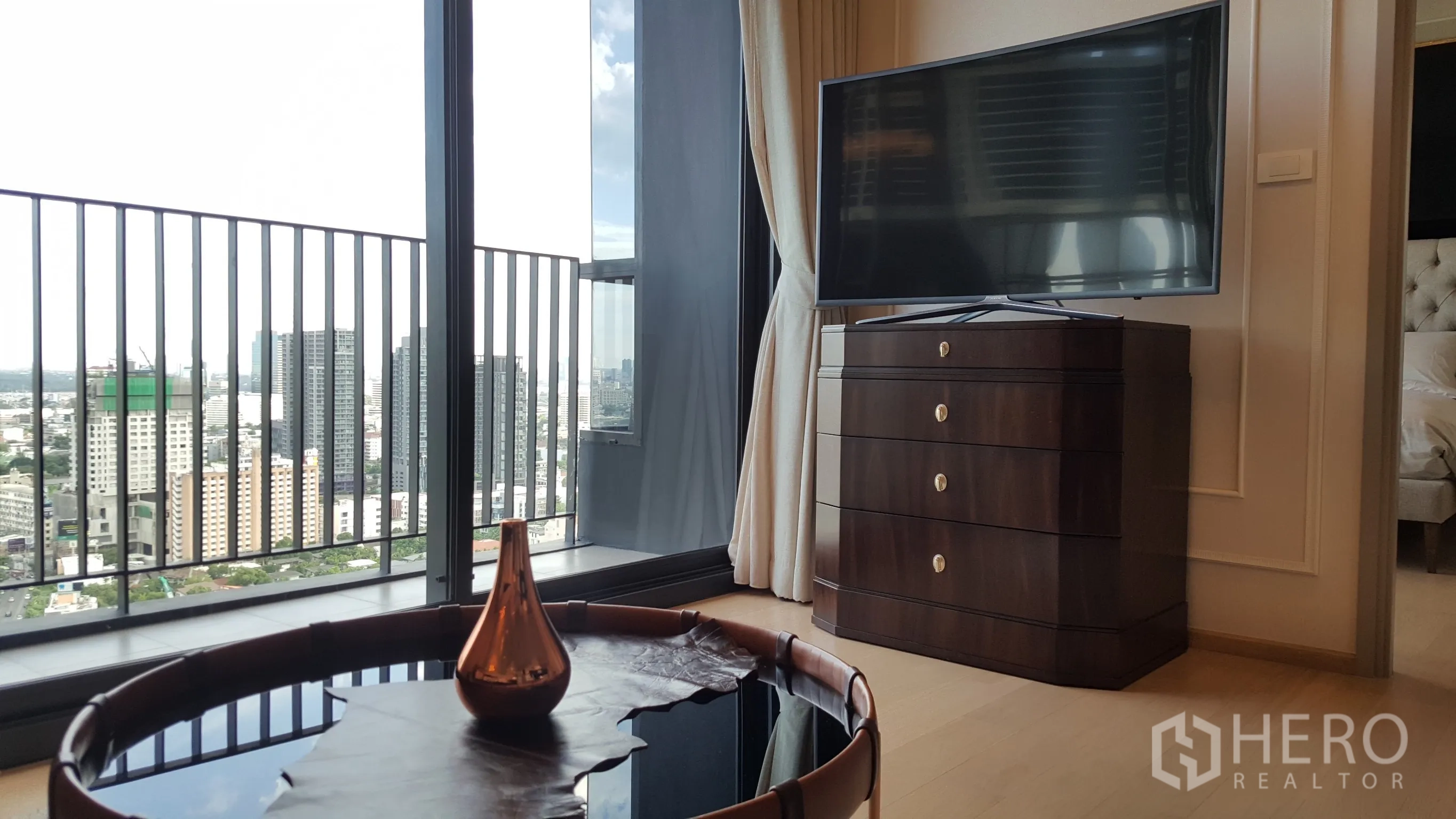 公寓 出租在Watthana, Bangkok - 客厅设落地窗与阳台，远眺城市天际线，深色电视柜与圆形茶几。