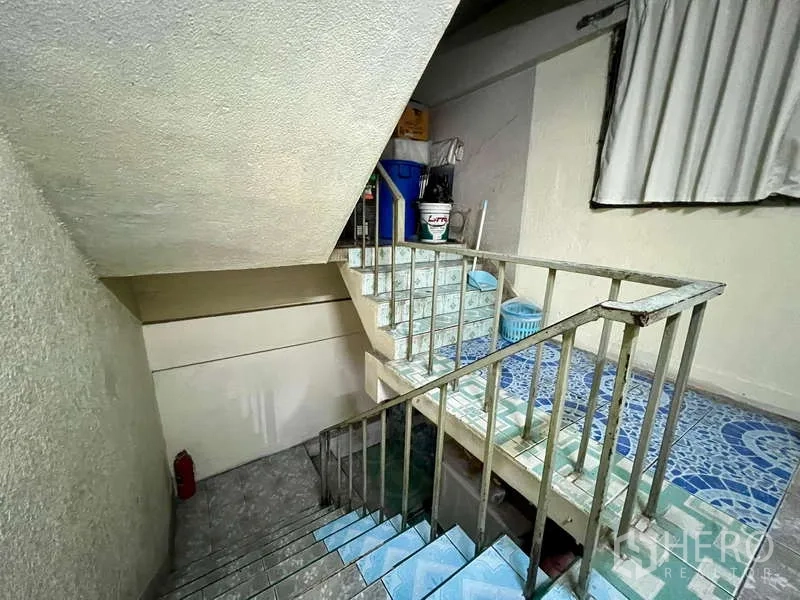 Shophouse for rent in Khlong Toei, Bangkok - Tiled internal staircase with metal railing and landing storage inside a multi-storey shophouse.