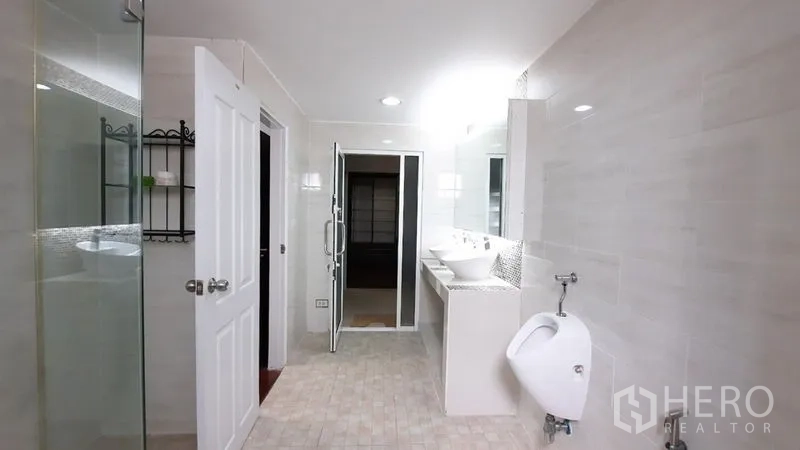 Townhouse for rent or sale in Suan Luang, Bangkok - Bright bathroom with double vanity, glass shower, and white tiles.