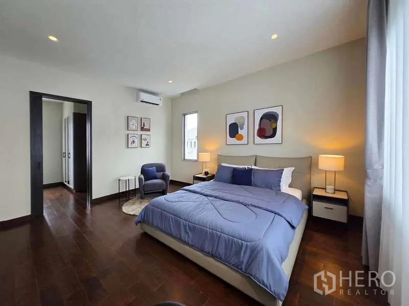 Detached House for rent or sale in Lat Krabang, Bangkok - Bedroom with blue bedding, corner armchair, and adjoining closet.