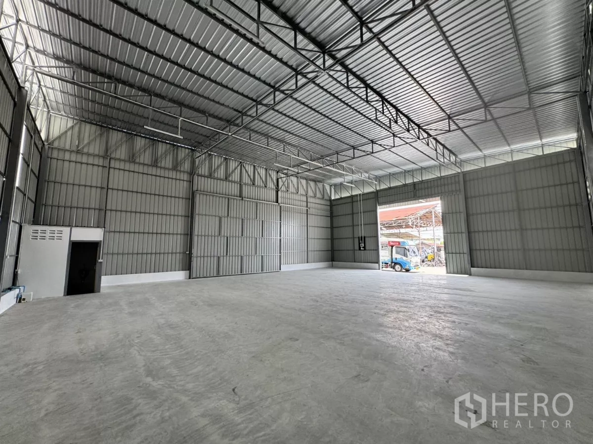 Warehouse for rent in Lam Luk Ka, Pathum Thani - Open warehouse bay with a tall street-facing loading door, bright metal cladding and smooth floors.