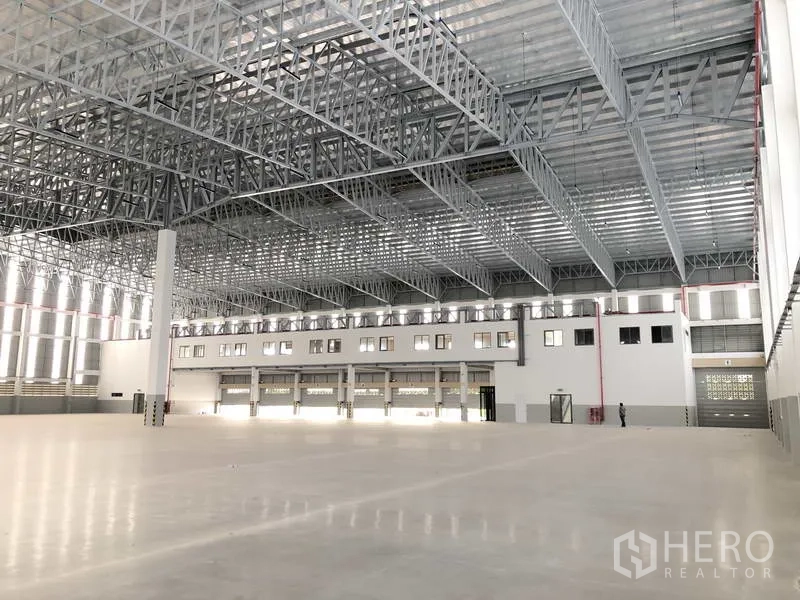 Factory for rent or sale in Samut Prakan - Warehouse hall with dock doors, mezzanine-style office windows, and safety markings.