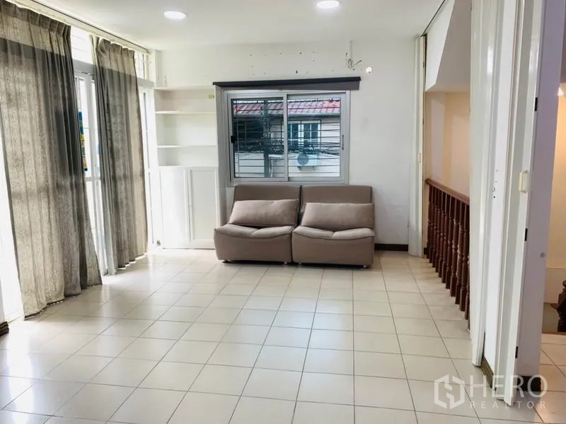 Townhouse for rent or sale in Huai Khwang, Bangkok - Upper-floor multipurpose room with tile flooring, sofa chairs, built-in shelves and balcony curtains