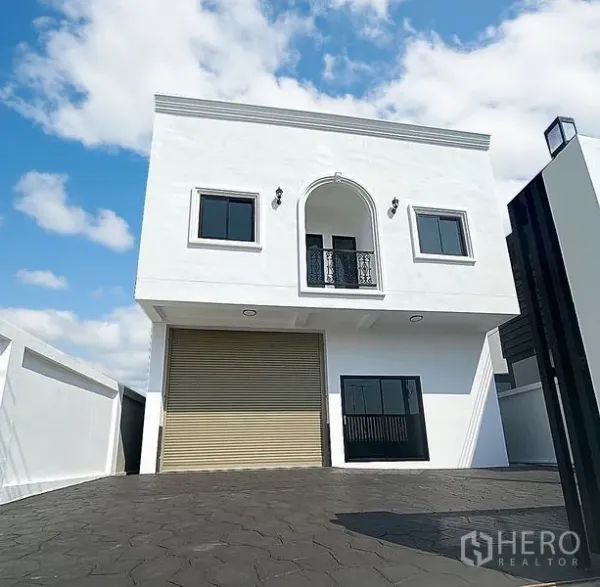 Warehouse for rent in Mueang Pathum Thani, Pathum Thani - Two-storey white warehouse with arched balcony, roller shutter door and gated driveway under blue sky.
