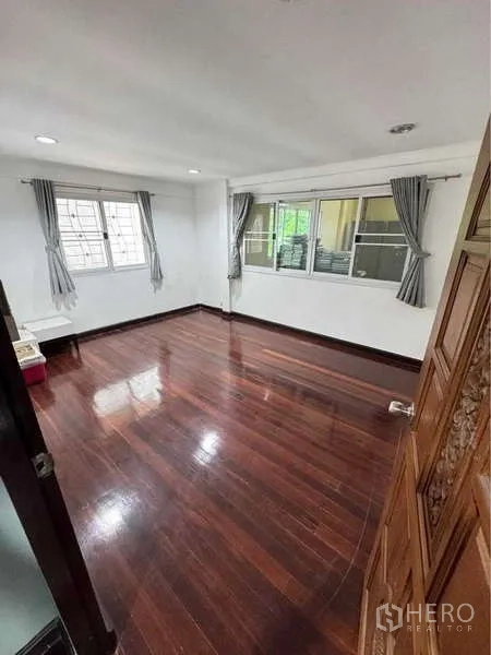独立式住宅 出租在Suan Luang, Bangkok - 采光充足的卧室，亮面木地板，两扇带窗帘的窗户。