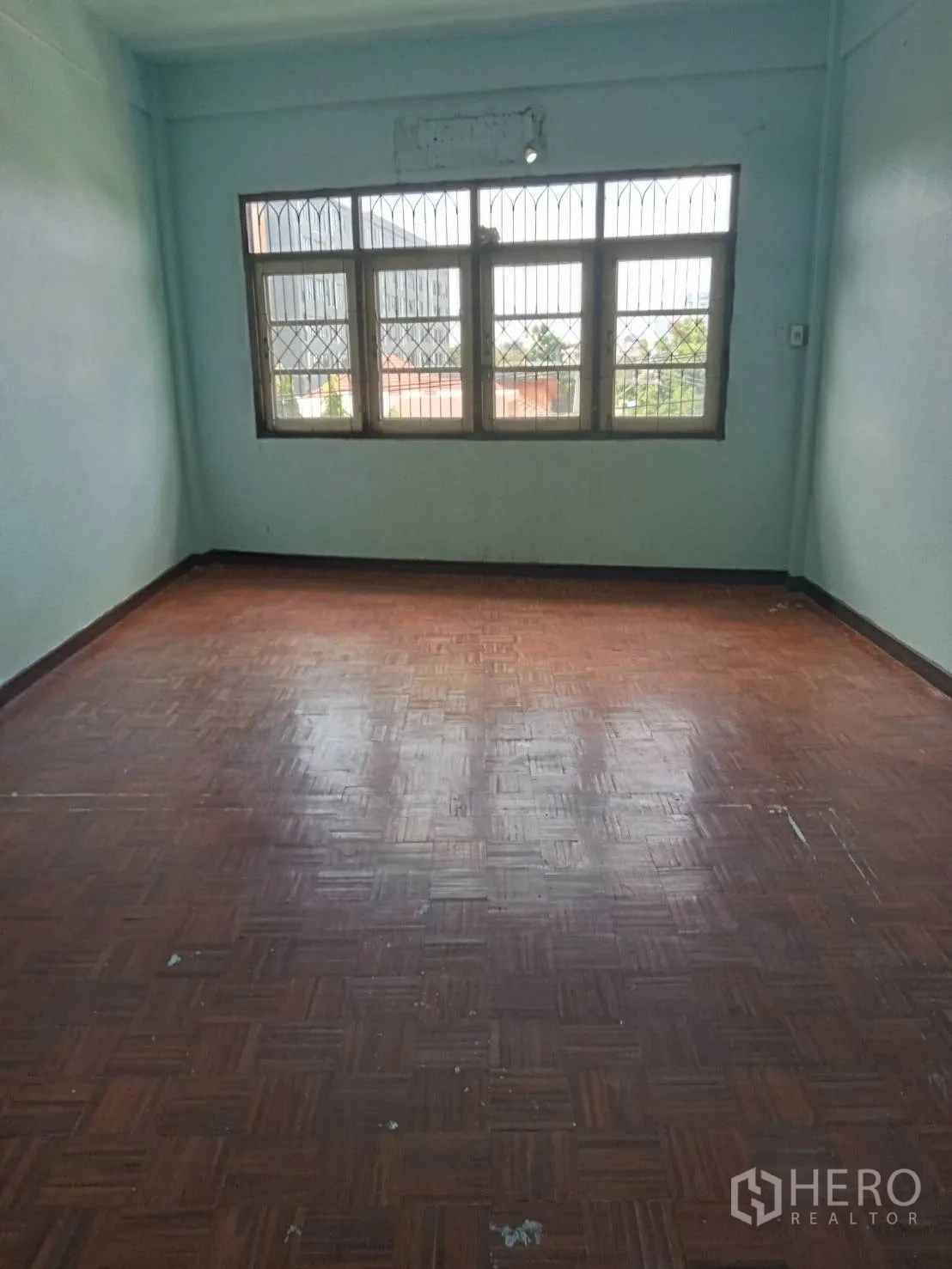Shophouse for rent in Phra Khanong, Bangkok - Bedroom with parquet flooring and large grilled windows overlooking the neighborhood.