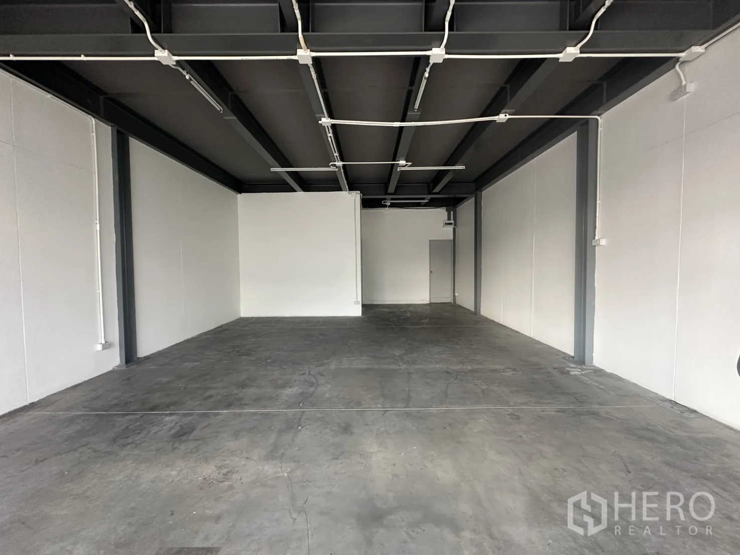 Retail Space for rent - Deep rectangular shop space featuring white walls, durable concrete floor, and surface-mounted lighting conduits.
