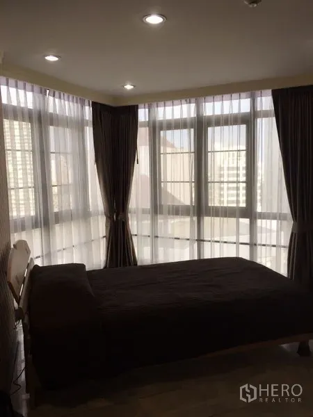 Condominium for rent in Watthana, Bangkok - Corner bedroom with floor-to-ceiling windows, sheer curtains and urban outlook.