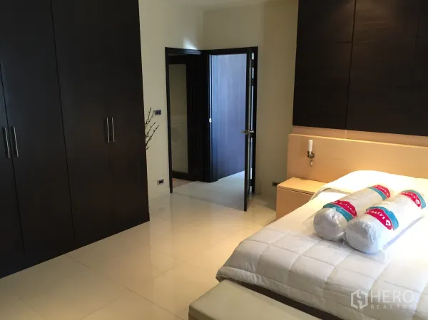 Condominium for rent in Bang Rak, Bangkok - Cozy bedroom with dark wood wardrobes, upholstered headboard and a doorway to the hall.