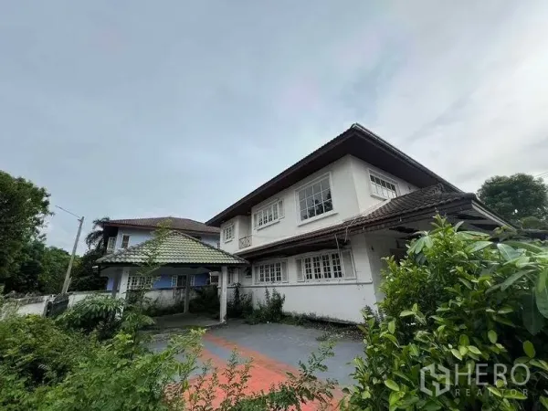 独立式住宅 出售在Phra Khanong, Bangkok - 前庭与车道通往两层住宅，带有有顶车棚与成树绿化。