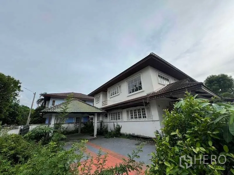独立式住宅 出售在Phra Khanong, Bangkok - 前庭与车道通往两层住宅，带有有顶车棚与成树绿化。