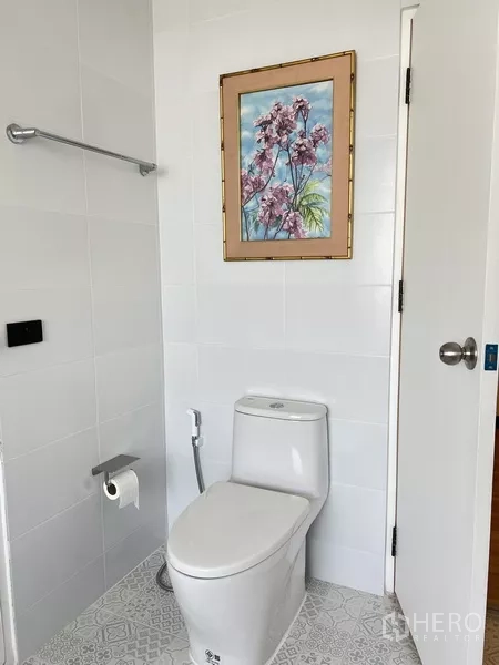 Condominium for rent in Khlong Toei, Bangkok - Clean bathroom with toilet, towel rail and framed floral artwork on the wall.