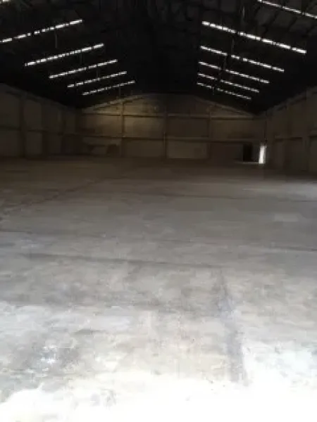 Warehouse for rent in Nakhon Pathom - Spacious warehouse interior with high steel truss roof, skylights, and smooth concrete floor.