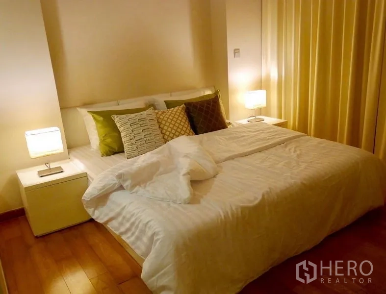 公寓 出售在Watthana, Bangkok - 温馨卧室，双人床、床头柜与暖色灯光，木地板。