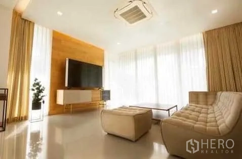Townhouse for rent in Huai Khwang, Bangkok - Sunlit living room with large TV console, modern sofa set and full-height curtains.