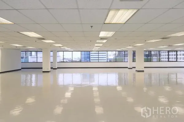 Office Space for rent in Bang Rak, Bangkok - Spacious open‑plan office floor with reflective tile, grid ceiling lights, and wide city‑view windows.