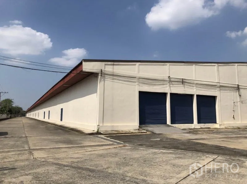 Warehouse for rent in Lam Luk Ka, Pathum Thani - Long side of the warehouse showing multiple loading docks with blue shutters and a truck ramp.