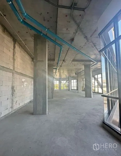 Retail Space for rent in Phra Khanong, Bangkok - Unfitted retail interior with high concrete ceiling, exposed blue piping, columns, and floor-to-ceiling corner windows.