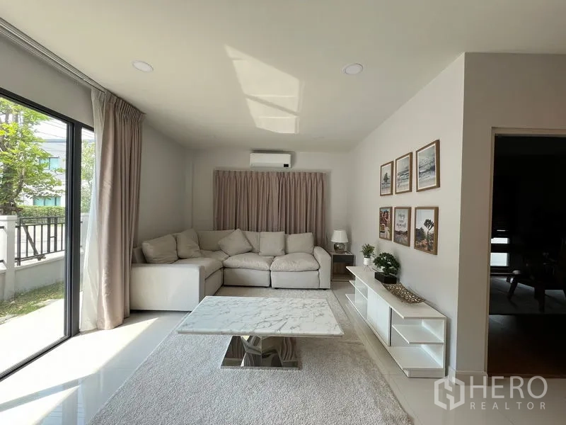 Detached House for rent in Bang Phli, Samut Prakan - Ground-floor living room with sectional sofa, large window and garden view.