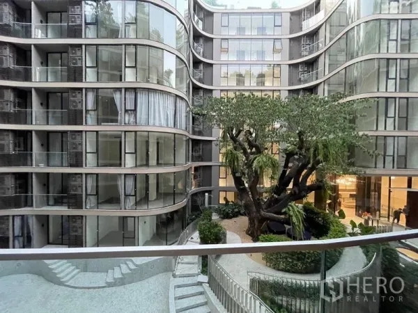 Condominium for rent in Khlong Toei, Bangkok - Curved glass condominium facade with landscaped courtyard and large tree