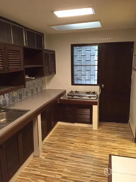 Detached House for rent in Watthana, Bangkok - Functional kitchen with wood louver cabinets, gas hob, tiled floor and window for ventilation.