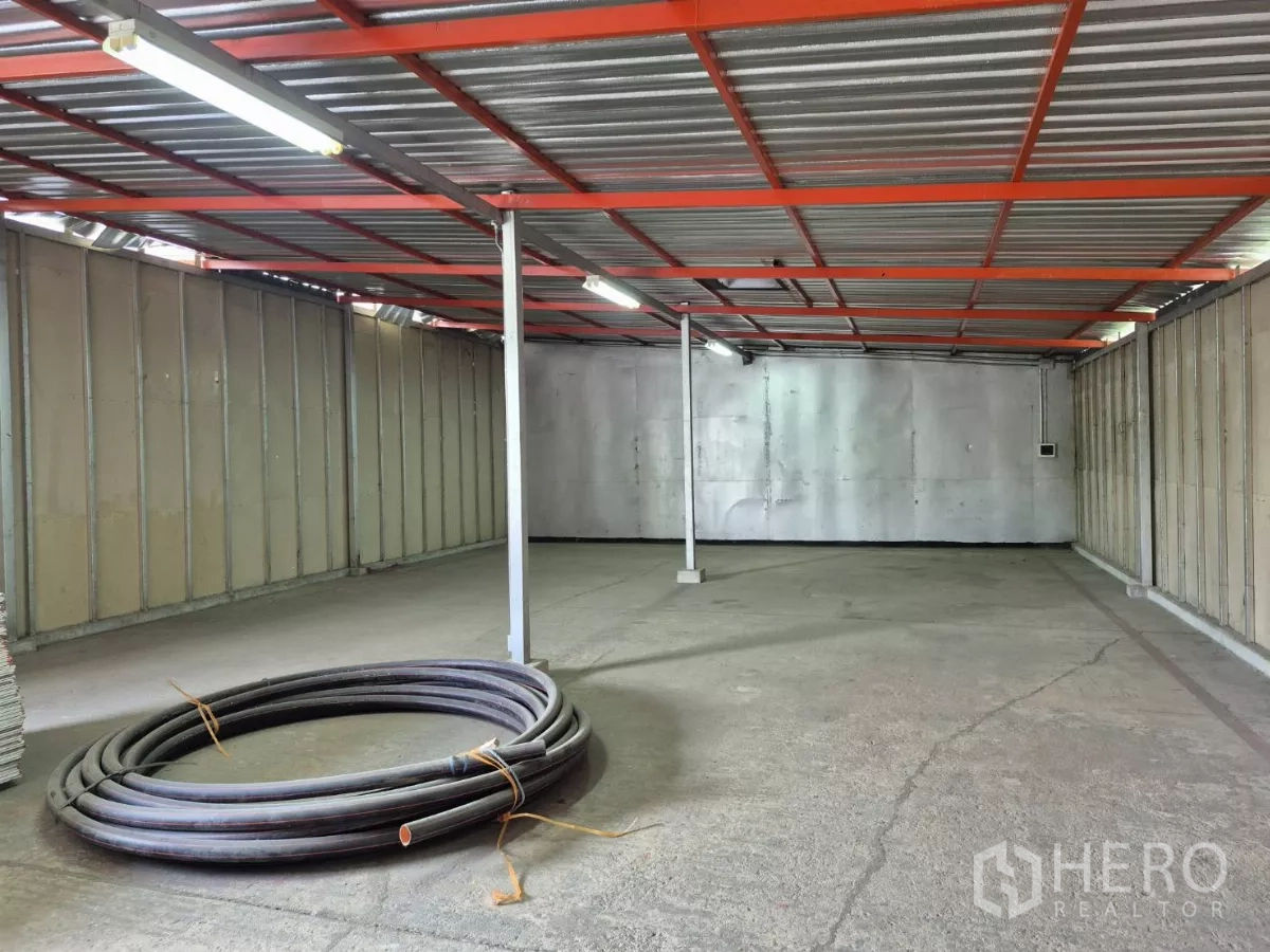 Warehouse for rent in Mueang Pathum Thani, Pathum Thani - Open-plan warehouse interior featuring a concrete floor, red steel roof frame and fluorescent strip lighting.