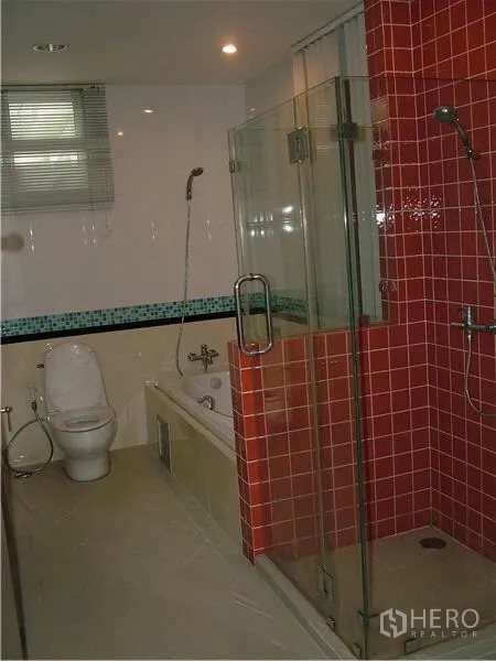 Condominium for rent in Khlong Toei, Bangkok - Modern bathroom with glass-enclosed shower, red accent tiles, bathtub, and toilet.