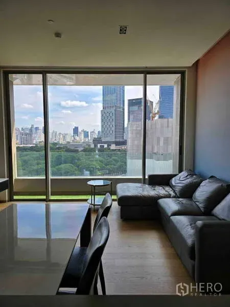 公寓 出租或出售在Bang Rak, Bangkok - 黑色皮沙发的起居区，面对巨幅窗户，可观赏曼谷天际线与绿意。