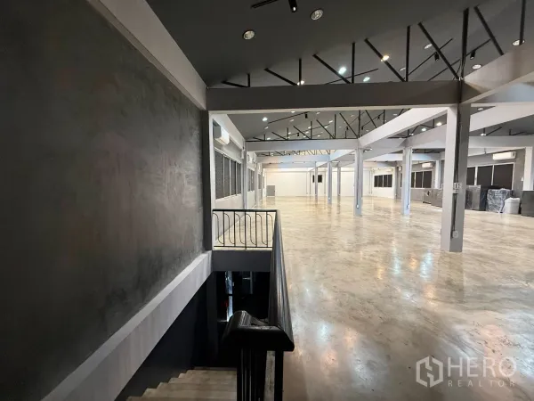 办公空间 出租在Wang Thonglang, Bangkok - 从楼梯平台望向宽阔大厅，工业风天花灯与开阔水泥地。