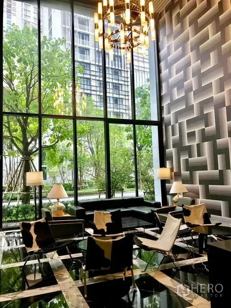 Condominium for rent in Khlong Toei, Bangkok - Elegant lobby with double-height glass, chandelier, stylish seating and views of a green garden courtyard.