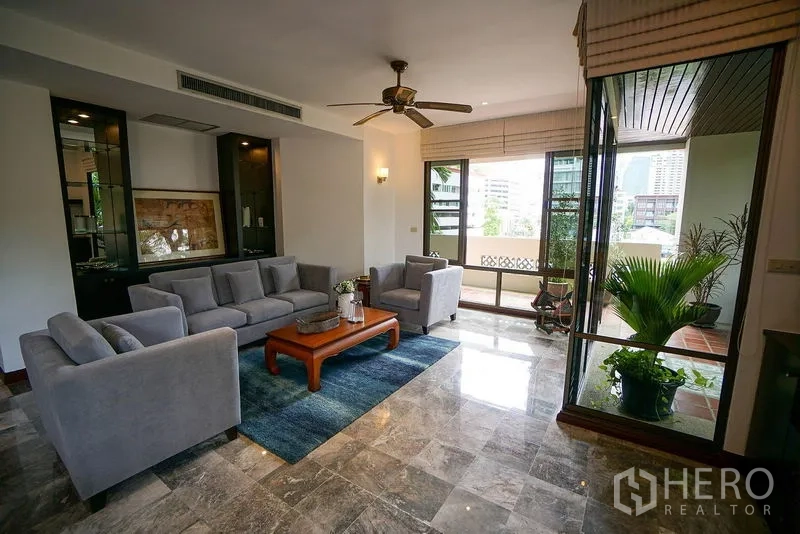 Apartment for rent in Watthana, Bangkok - Bright lounge with large windows, city glimpses, and a balcony with potted plants off the sitting area.